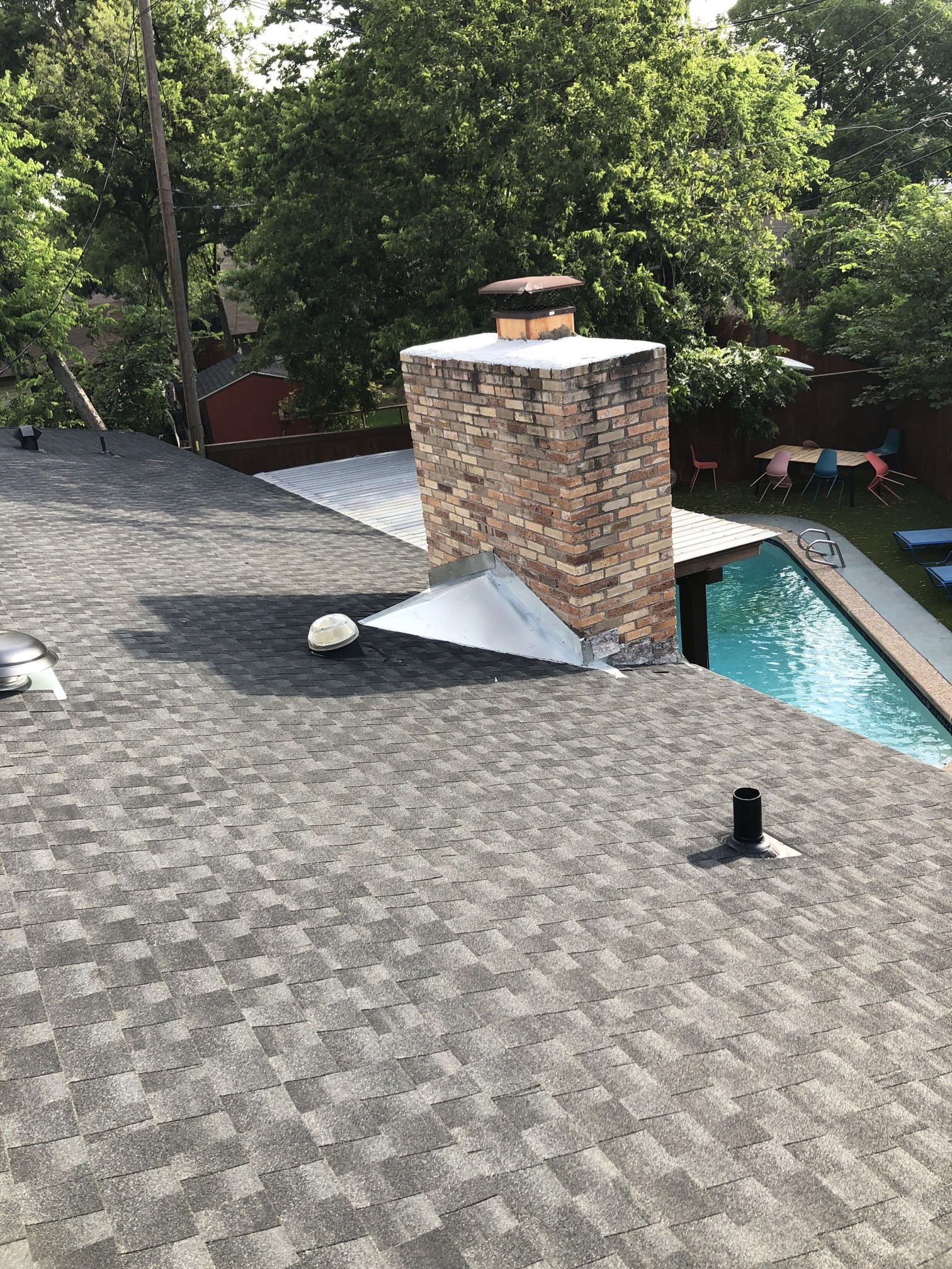 Wide view of a metal cricket and brick chimney on a gray shingle roof.