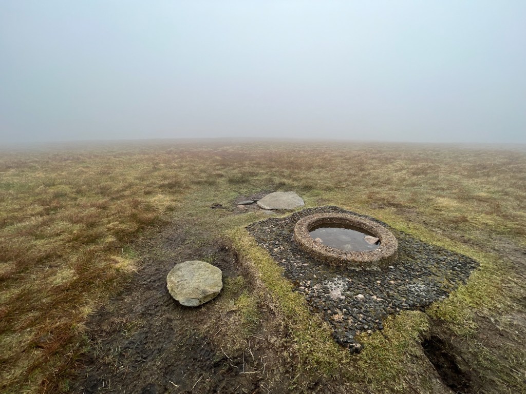 A small, flat circle cain made of a gravel-concrete lays on the floor surrounded by grass. In the distance is thick fog with no views.