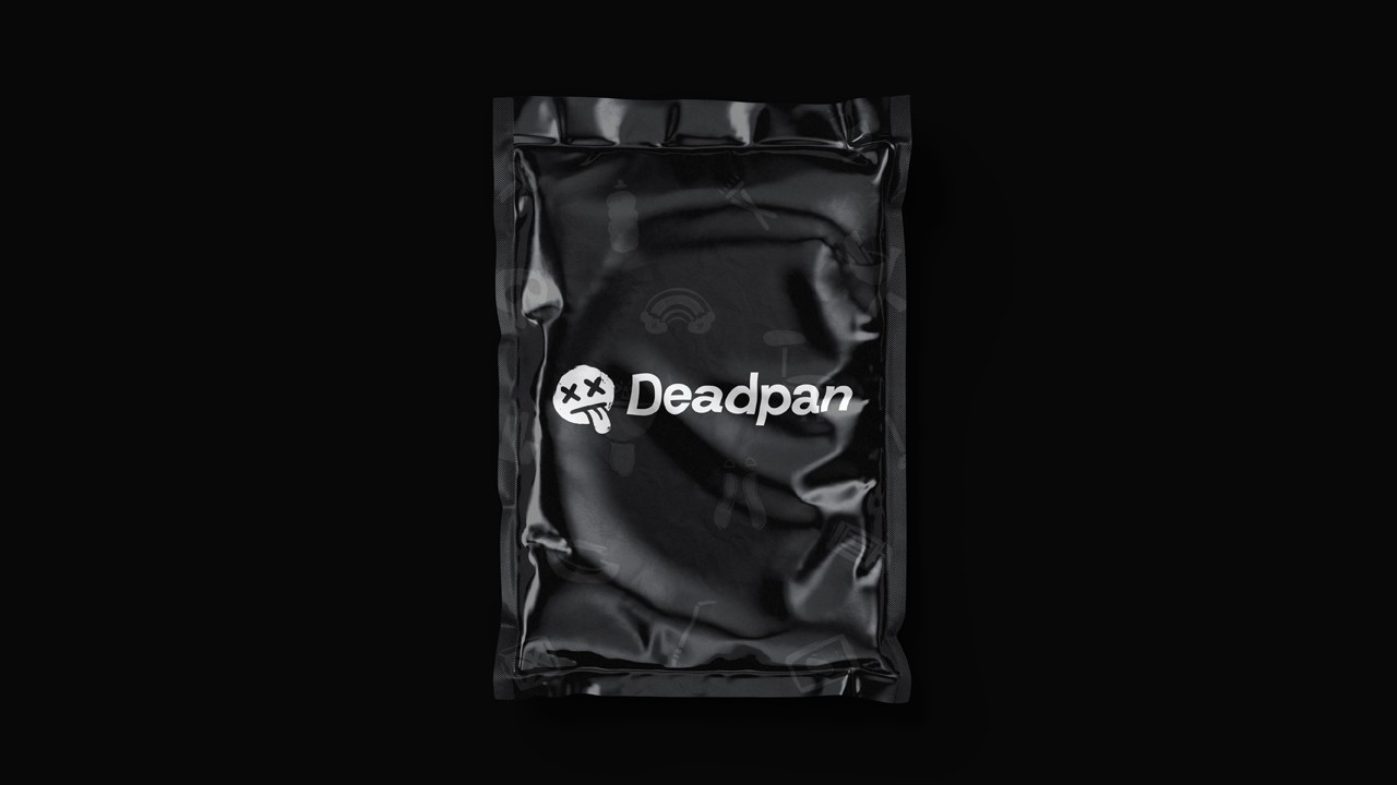 Black metallic foil pouch photographed from above, printed with a glossy white distressed smiley face logo (X eyes, tongue out) in the centre, faintly showing small white icon patterns beneath.