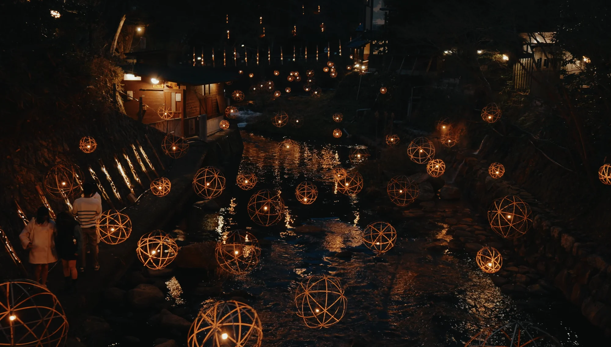 Woven bamboo lantern spheres glowing along the Tanohara River at dusk during the Yuakari illumination