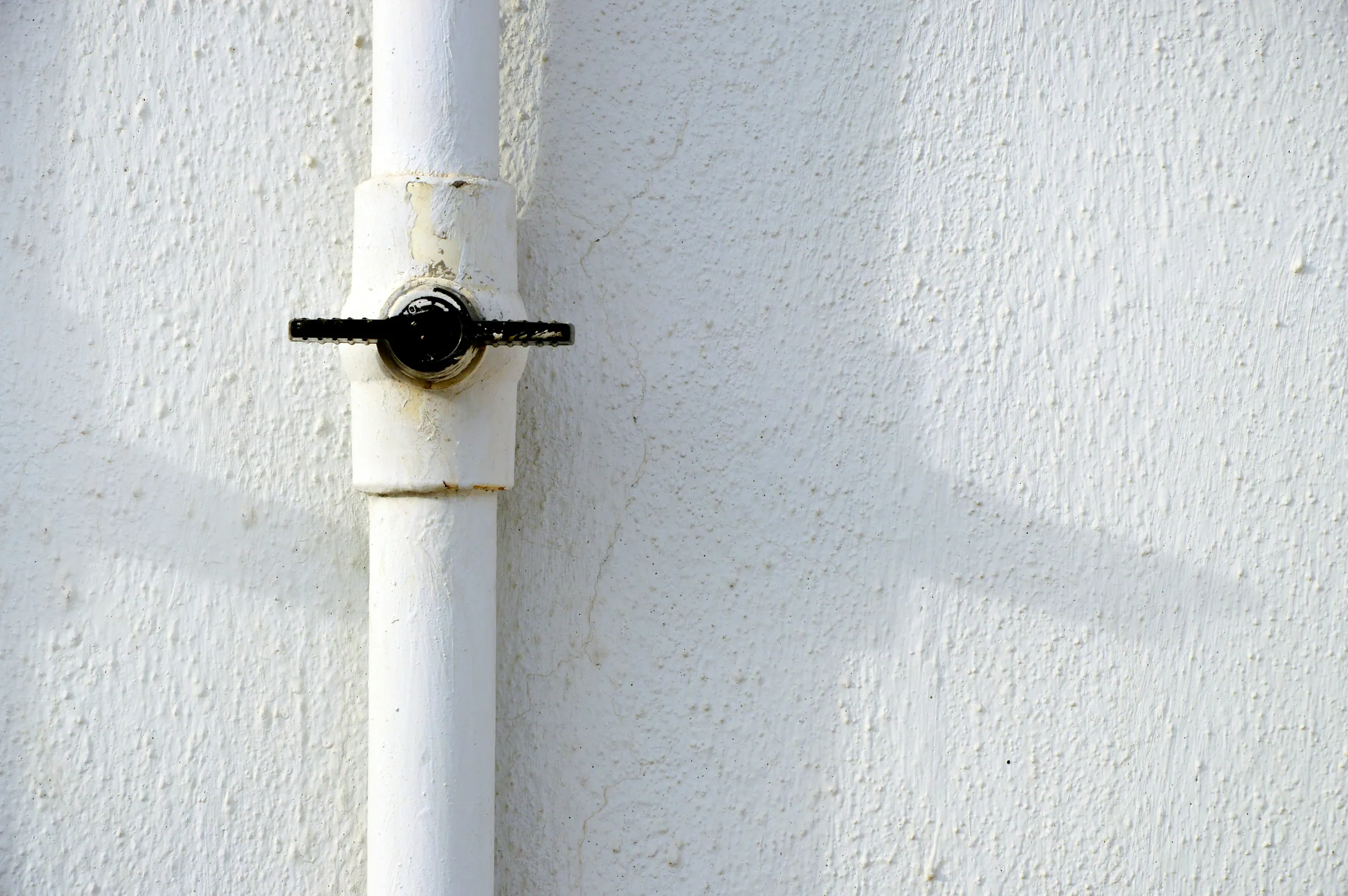 White water pipe with a shut-off valve on a white wall