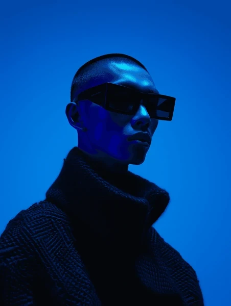 Close-up of a person wearing rectangular sunglasses illuminated by deep blue light.