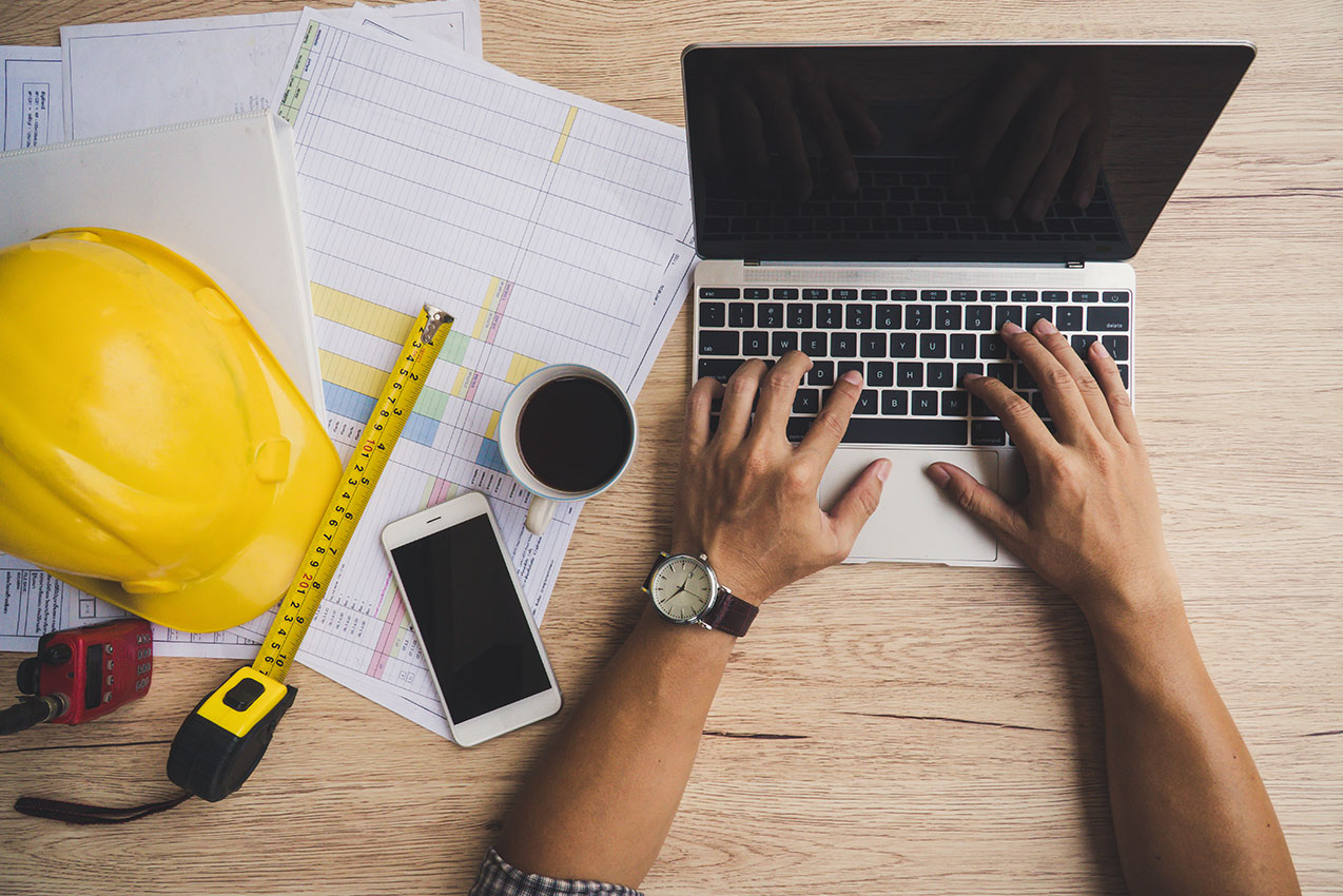 Ansicht von oben auf Person, die am Laptop arbeitet, und Bauequipment daneben