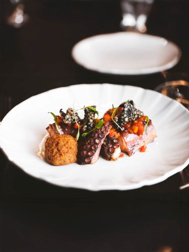 Close-up of an elegant plated dish featuring octopus, a savory crumble, and a vibrant red sauce.