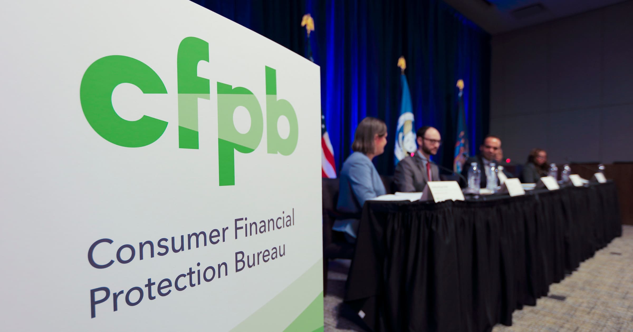 Image of Consumer Financial Protection Bureau meeting, logo in foreground