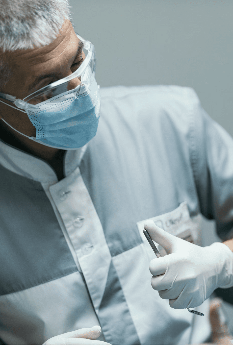 Стоматолог у захисній масці та окулярах схвалює результат лікування, консультує усміхнену пацієнтку, яка сидить у стоматологічному кріслі.