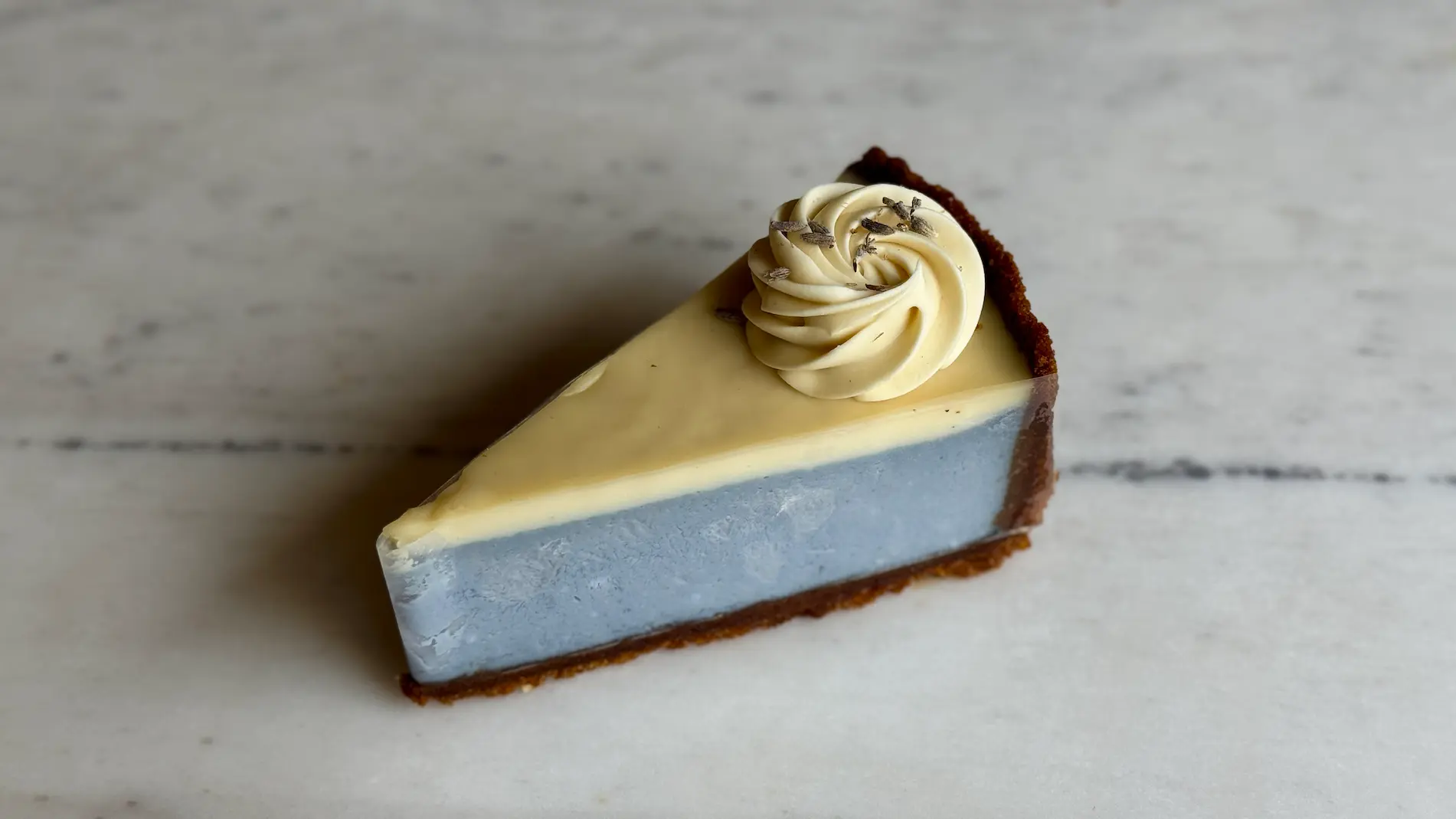 Two-tone cheesecake slice with blue and yellow layers, topped with white chocolate rosette
