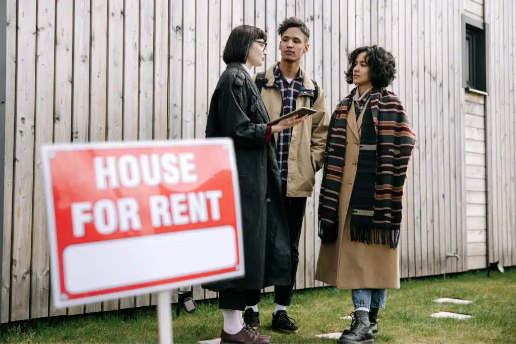 Landlord property management depicted by a leasing agent discussing rental details with prospective tenants beside a house for rent sign.