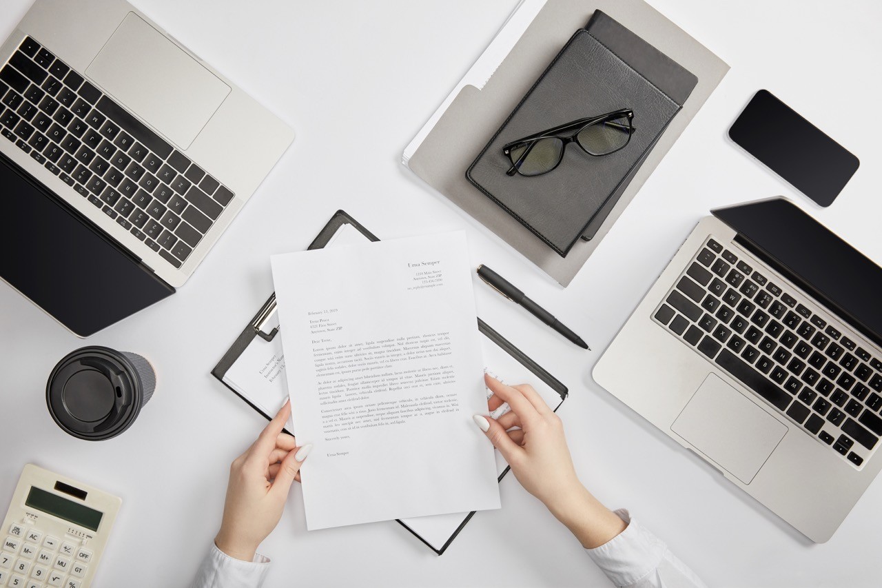 Hands holding a legal document surrounded by laptops and office tools, representing SAA Law's comprehensive dispute resolution services in Saudi Arabia.