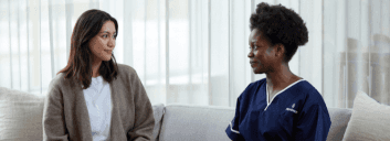 Florence care worker and woman sitting together and talking on a sofa.