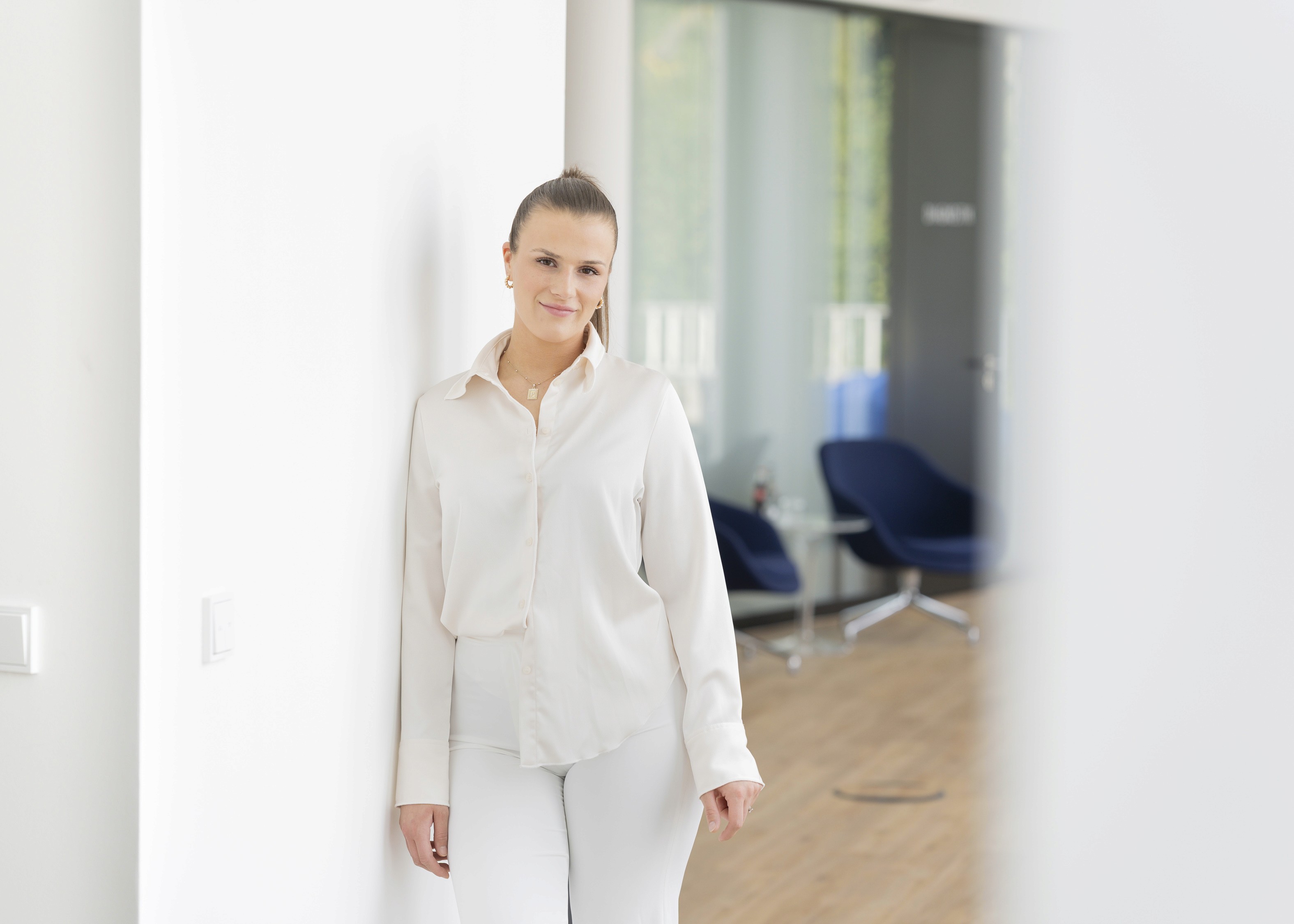 Freundliche Mitarbeiterin lehnt entspannt an der Wand in moderner Praxisumgebung