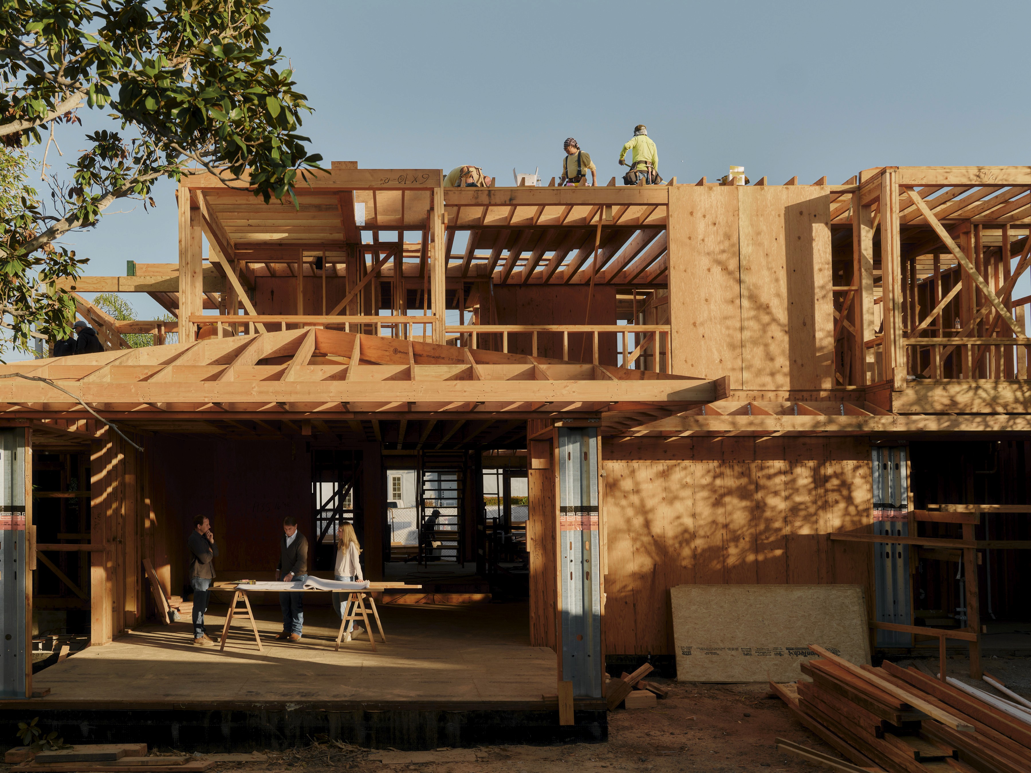 Three owners stand outside a modern two-story home, with one person pointing toward the house’s exterior features during a walkthrough.