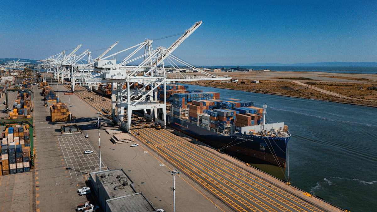 Large cargo ship docked at the quay with white port cranes performing loading operations.
