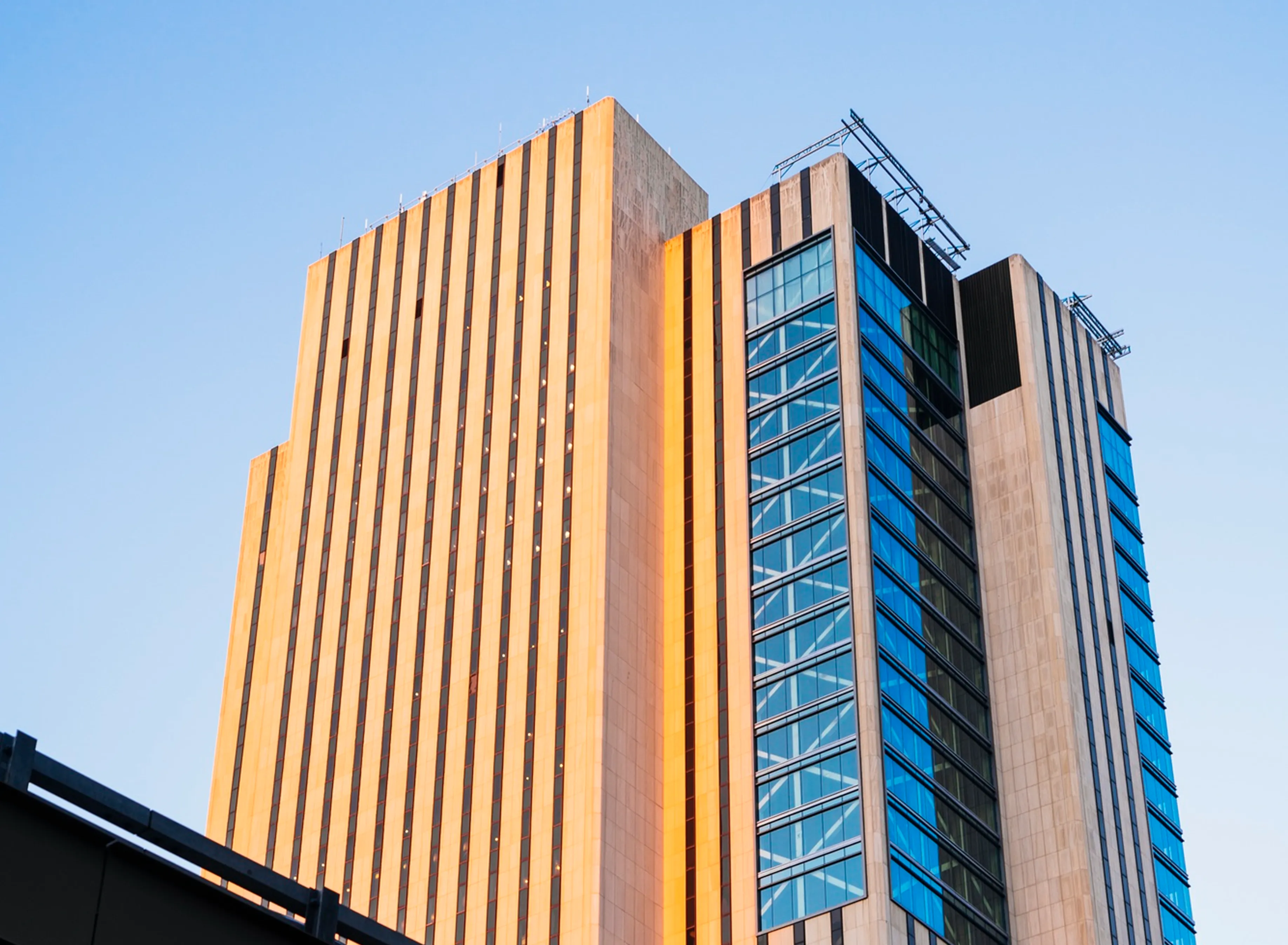 Modern skyscraper with vertical architectural fins and glass windows against a clear blue sky.