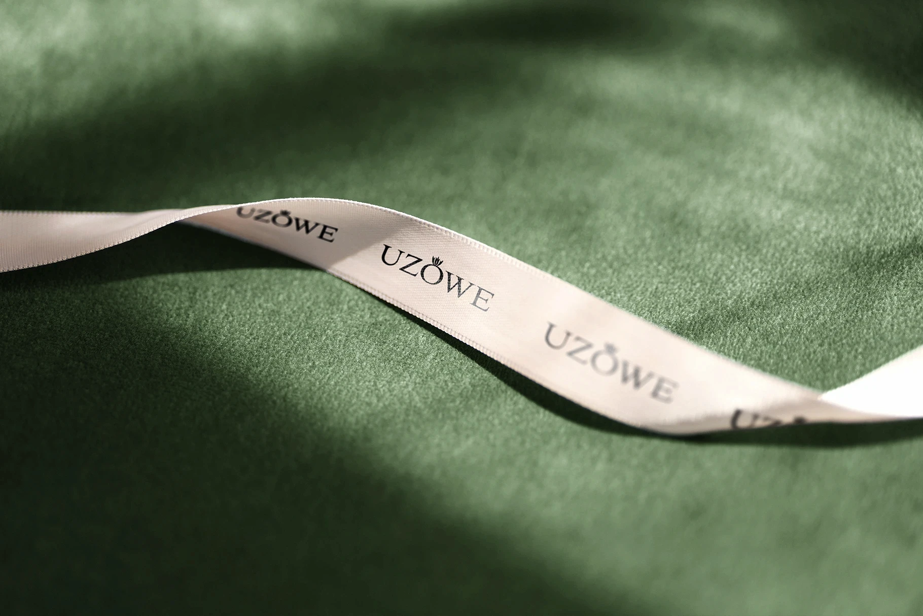 Luxury ribbon lace mockup with a repeating logo on a textured green velvet surface.