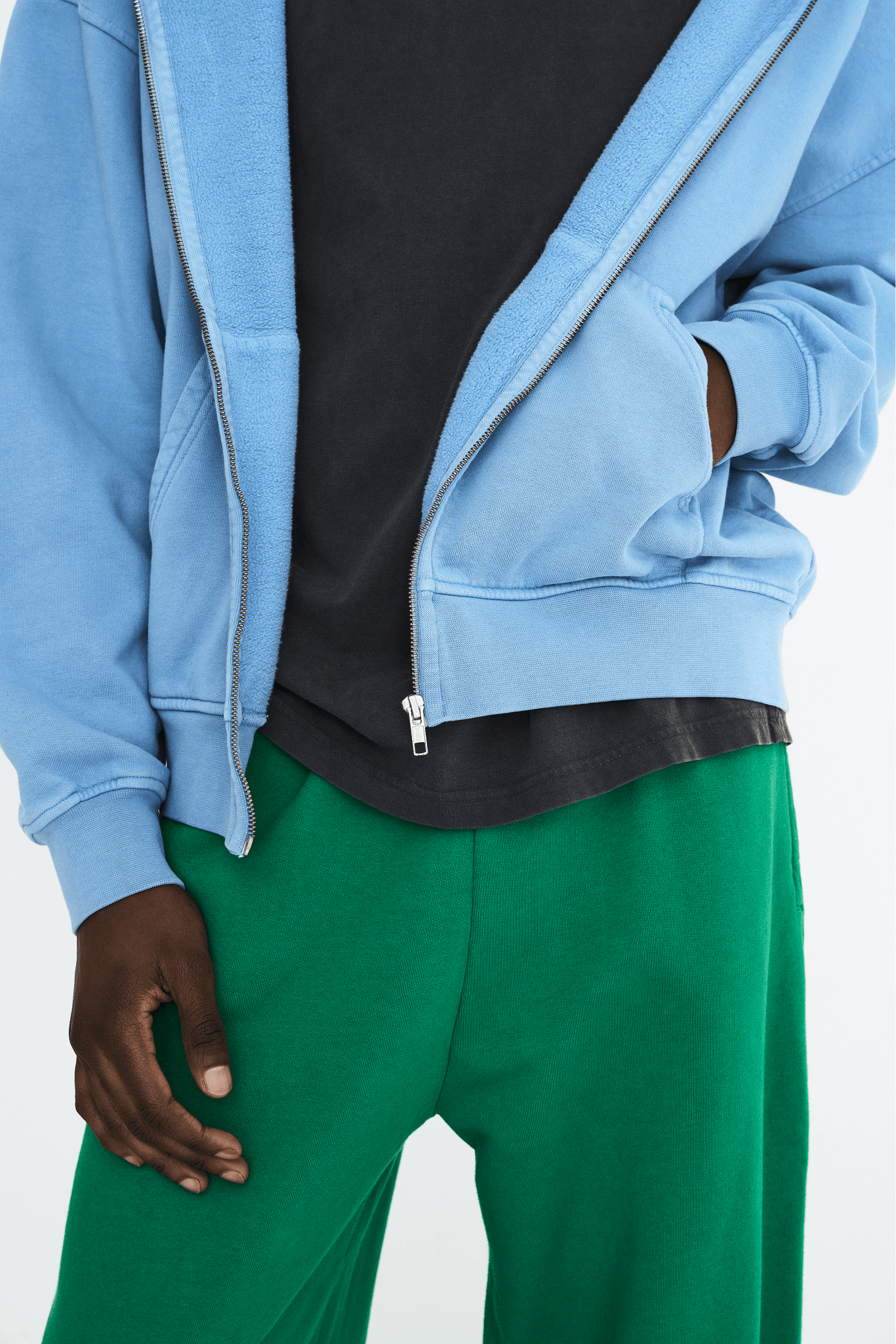 Détail de look avec sweat-shirt à capuche bleu ciel, pantalon vert et t-shirt noir