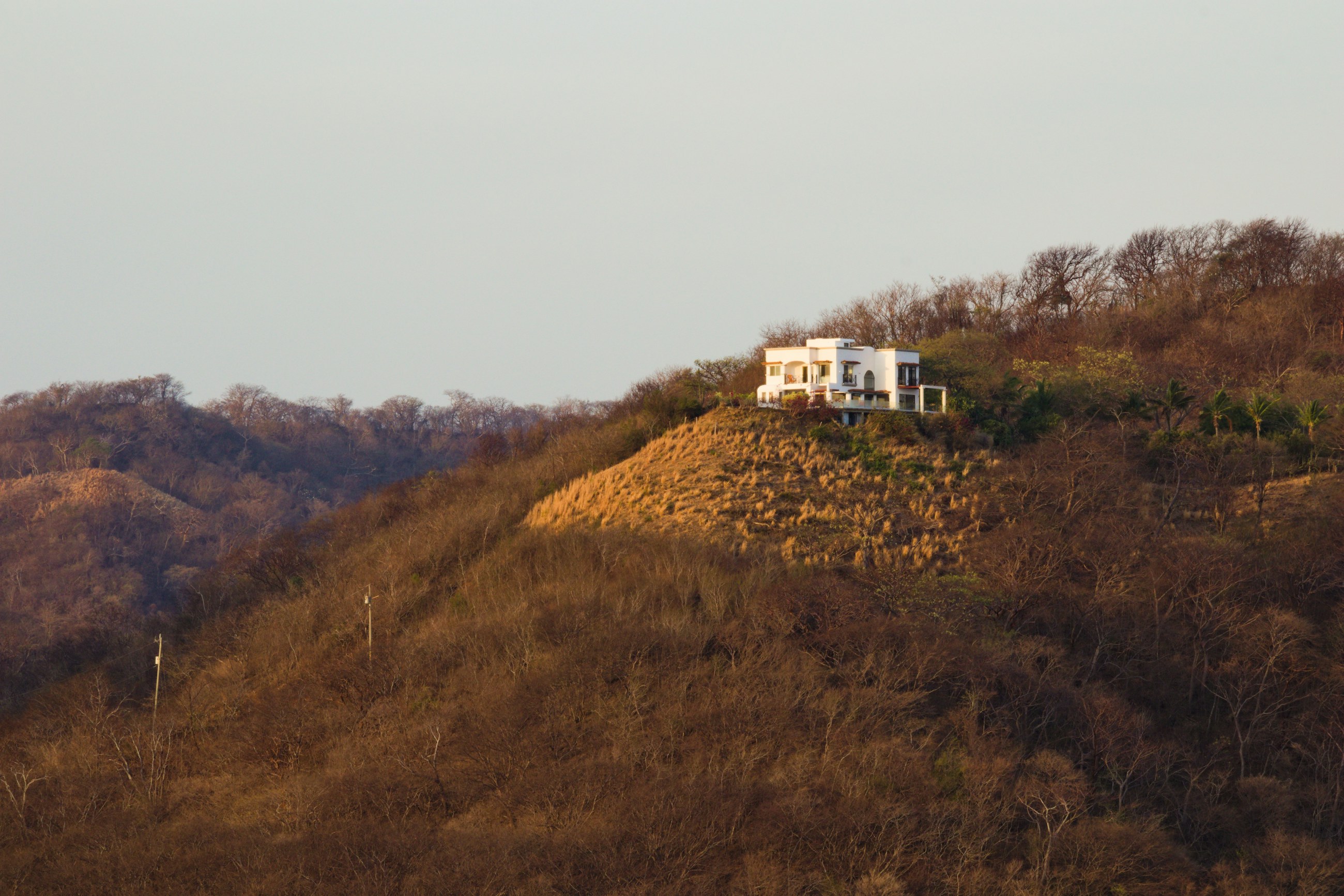 White two-storey house on a hilltop, slopes of dry brown scrub in low sun