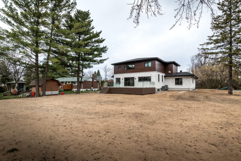 Modern two‑storey home with dark upper and light stone‑clad lower exterior, paved front walkway and large windows showcasing the high‑end residential properties serviced by B&Y Reno Corp