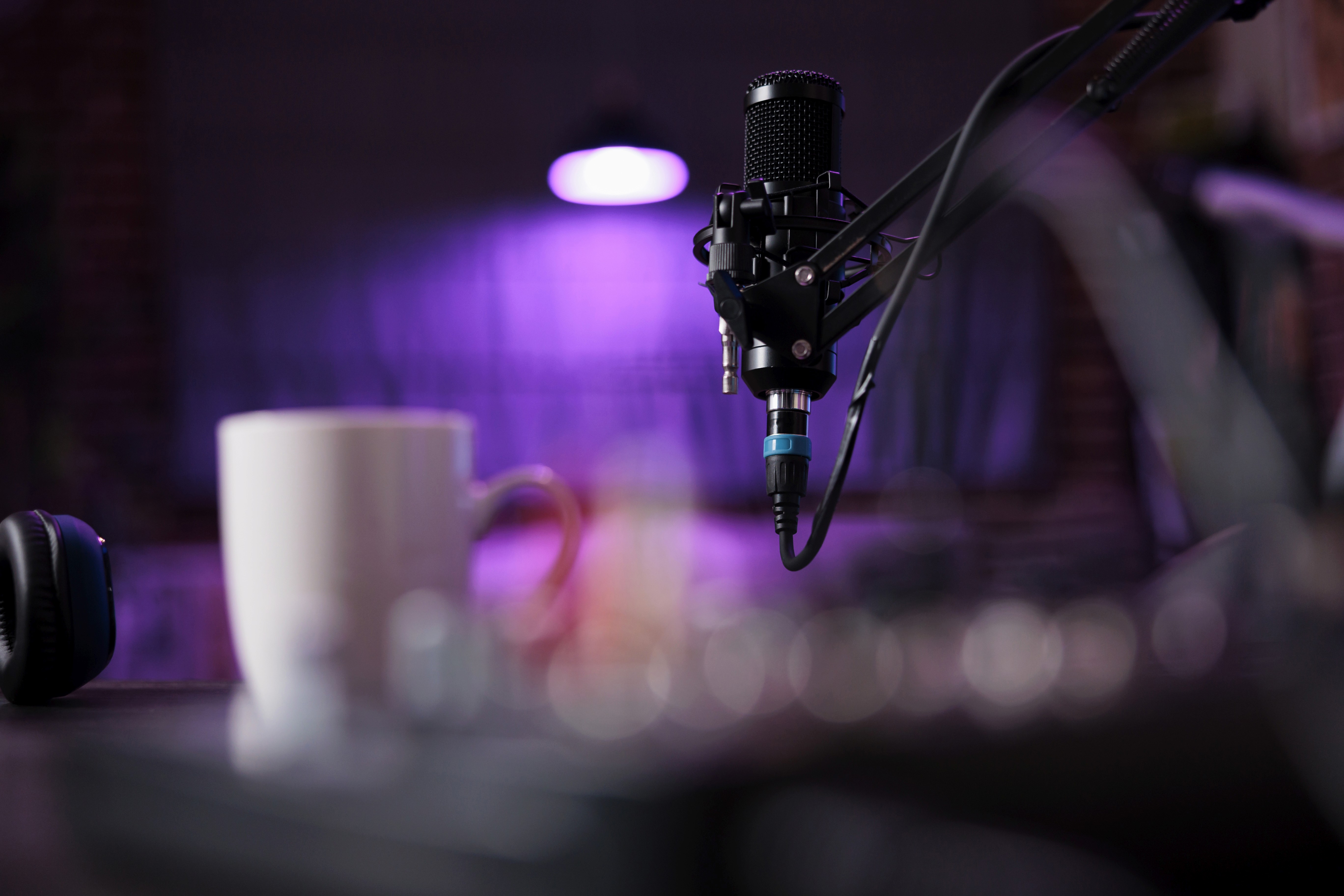 A professional condenser microphone on a boom arm in a modern podcast studio with purple neon lighting. This visual highlights Woody Vision’s role in helping podcasters and social creators discover and verify trending user-generated content (UGC) for their digital broadcasts.