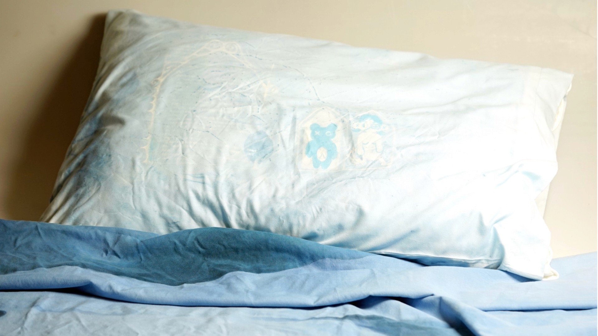 a white pillow on a bed with a blue comforter.