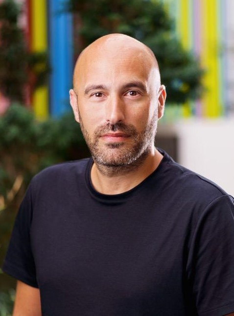 Smiling young man in a black t-shirt against a gray background, radiating warmth and friendliness.