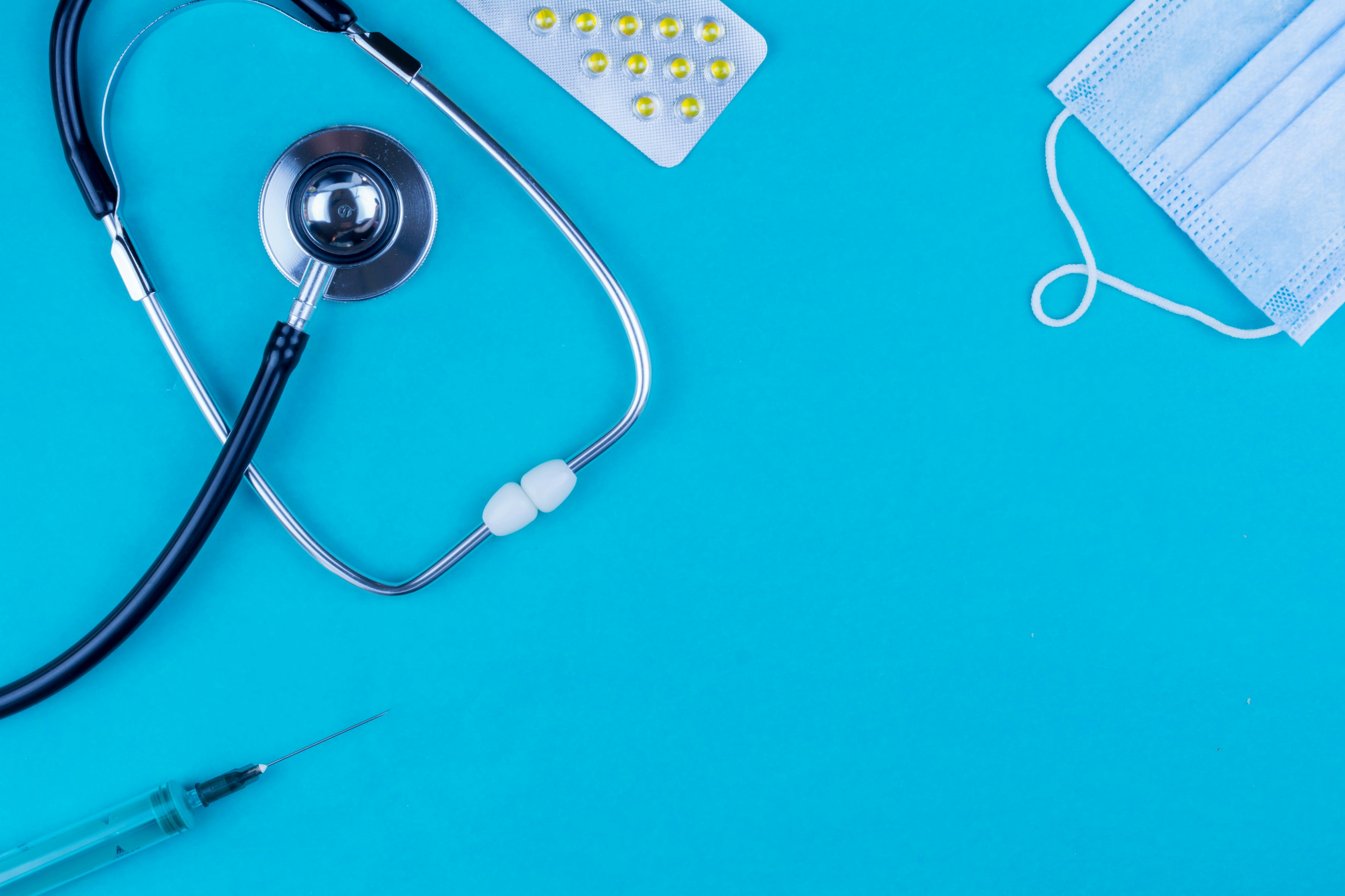 Stethoscope, mask, syringe, and pill packet on a aqua green table