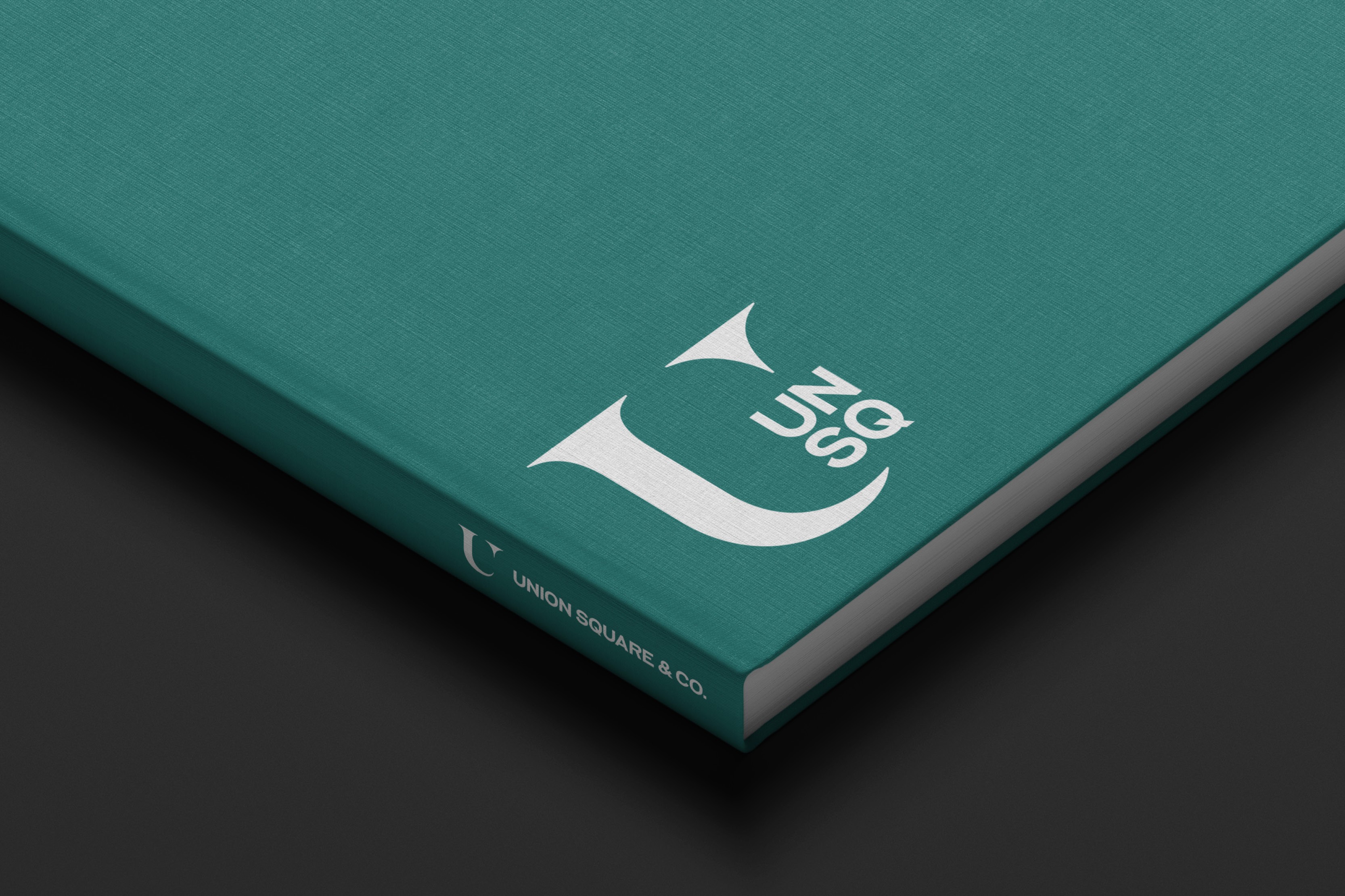 A close-up of a teal surface featuring a stylized white logo of Union Square & Co. at the corner.