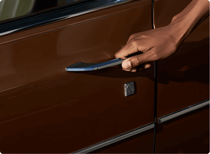 A hand is reaching for the chrome door handle of a classic vintage brown car, highlighting the vehicle's polished exterior and sleek design.