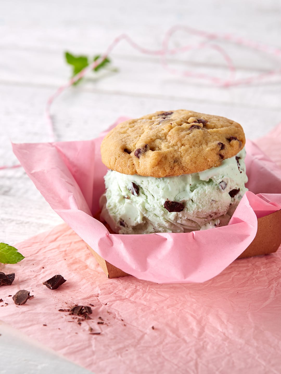 Mint chocolate chip ice cream sandwich in chocolate chip cookies, pink parchment on white table