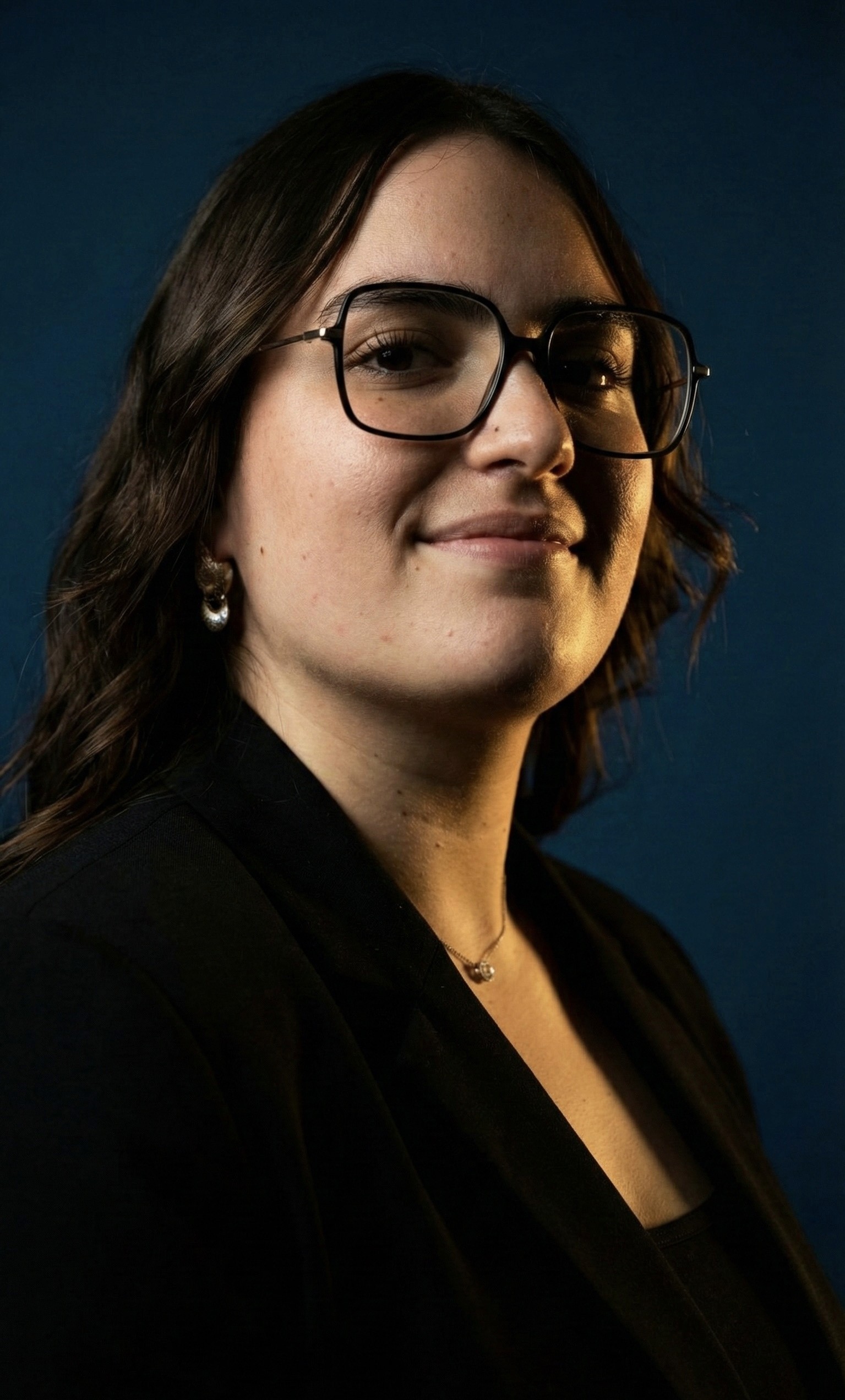 Smiling young woman with curly hair sitting at a laptop, in front of a teal wall.