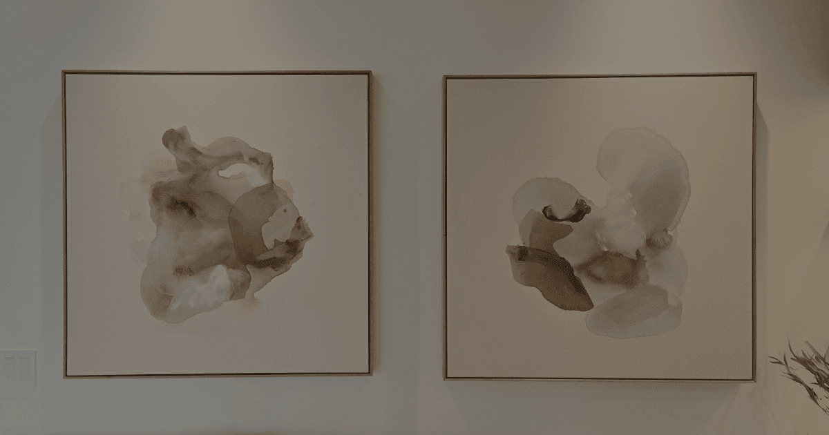 Two coordinating square pieces of neutral abstract water colour art sit on a wall.