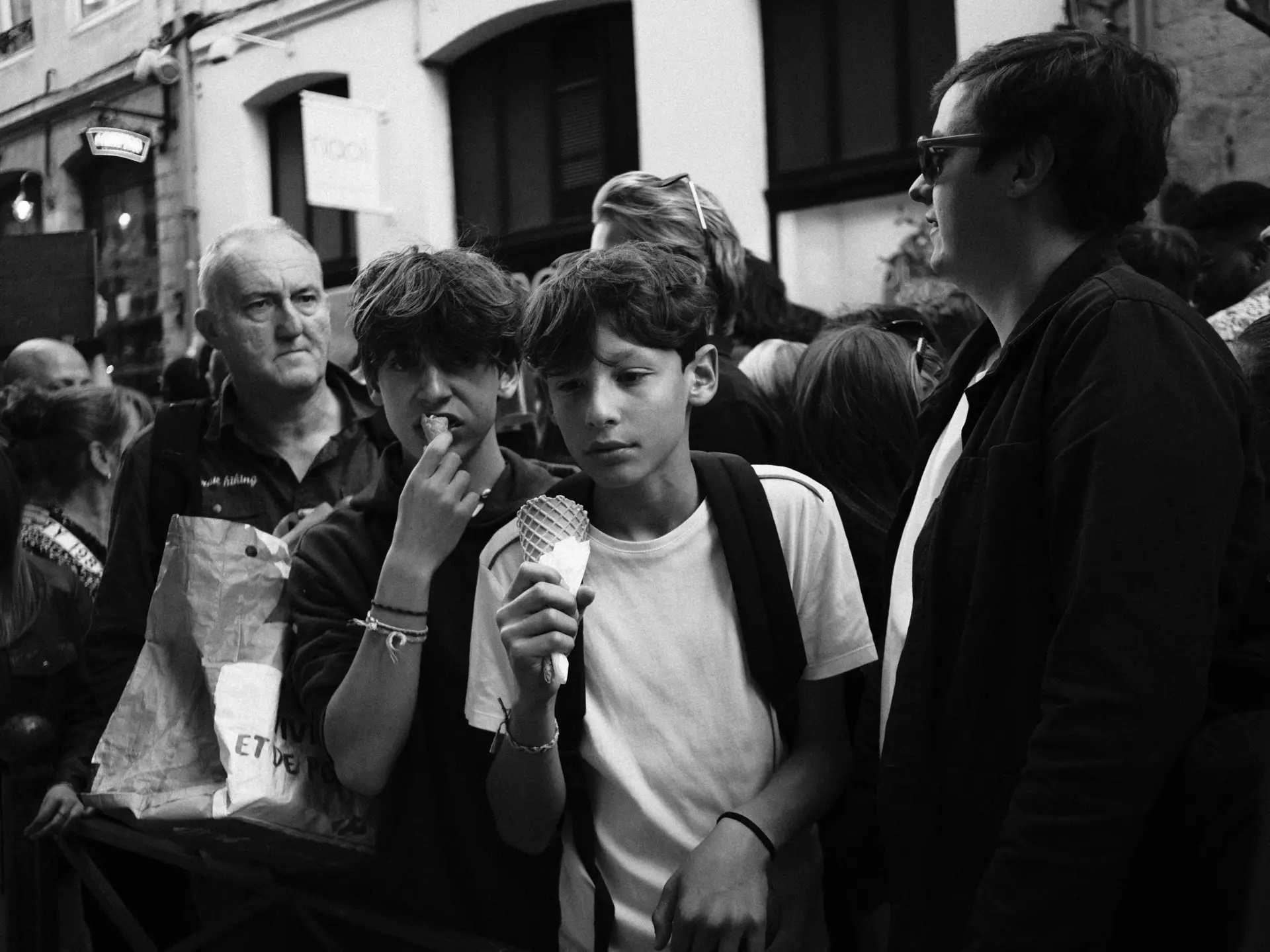 Boys eating ice cream in a crowd, in black and white