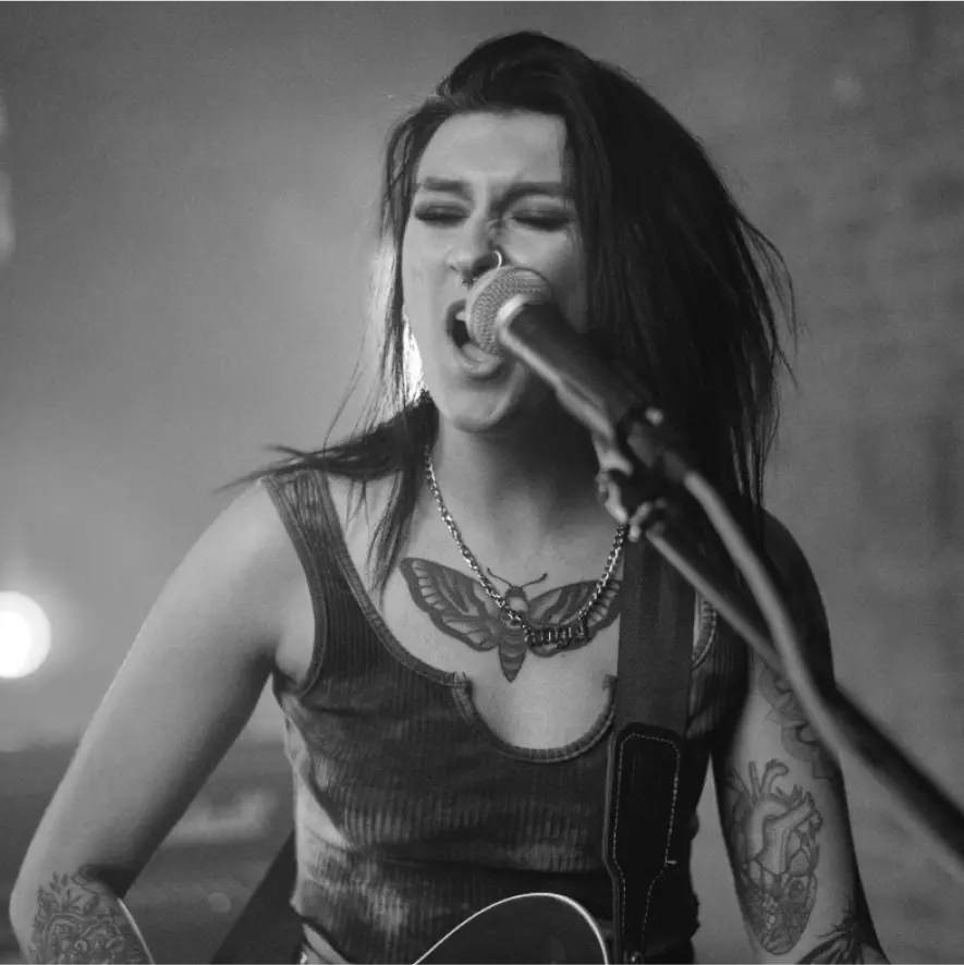 A vocalist with a piercing is passionately singing a rock song while playing the guitar and holding a microphone.