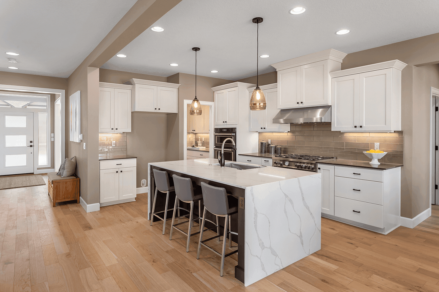 A balanced kitchen design featuring white shaker-style cabinets, a marble island with seating, and warm beige walls. Modern pendant lights and stainless steel appliances provide contemporary touches in this versatile space.