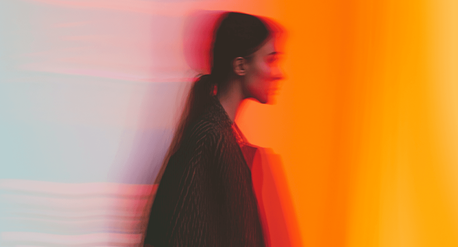 A black and white portrait of a woman set against a vibrant orange background.