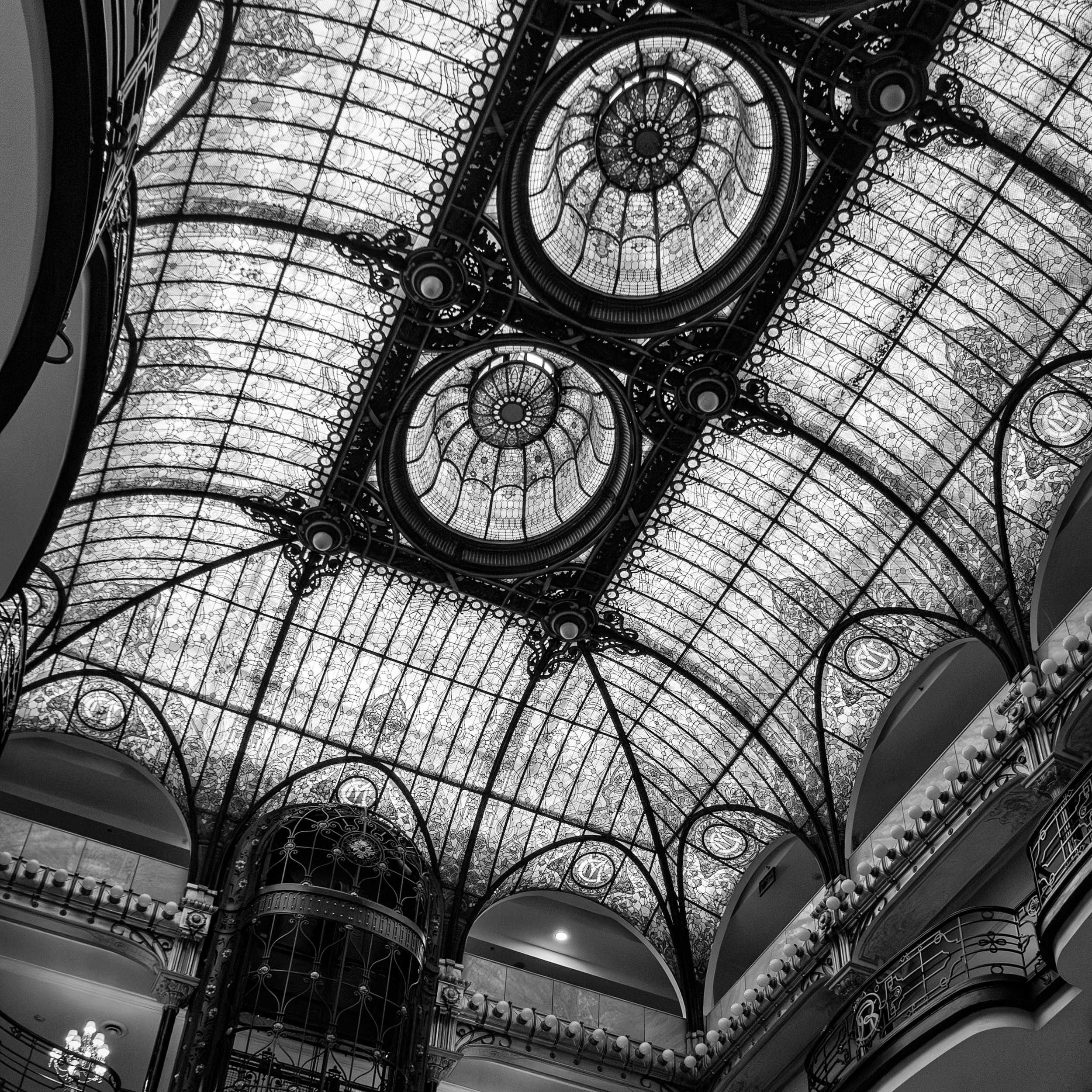 Black and white photograph of the ornate stained glass ceiling at Gran Hotel Ciudad de México, featuring ironwork and symmetrical domes in Art Nouveau style.