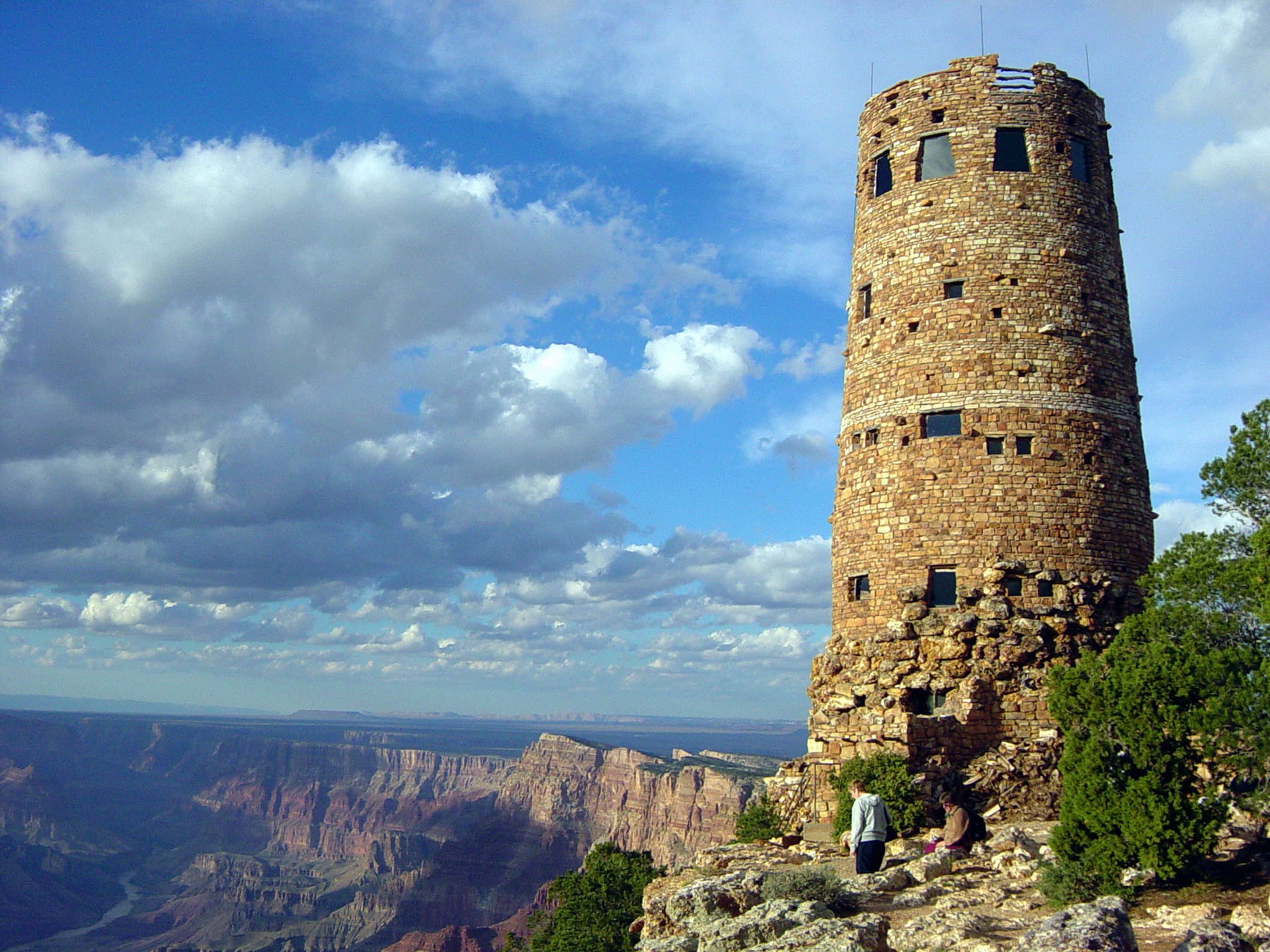 The stone Desert View Watchtower standing on the edge of the South Rim, with the Grand Canyon and a bend of the Colorado River far below to the left.