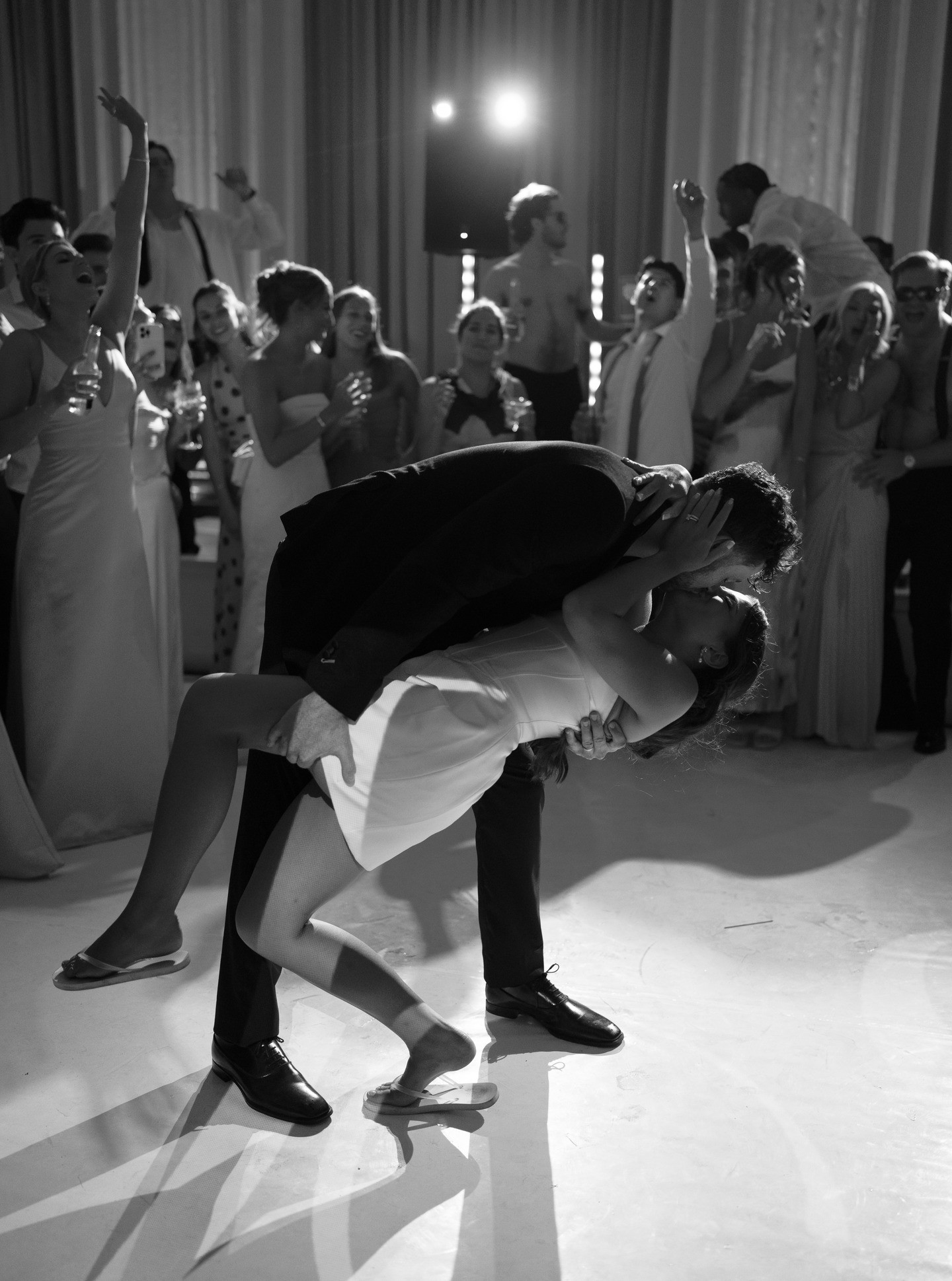 A couple dances closely, showcasing a flowing green dress, against a soft, blurred background of other guests.