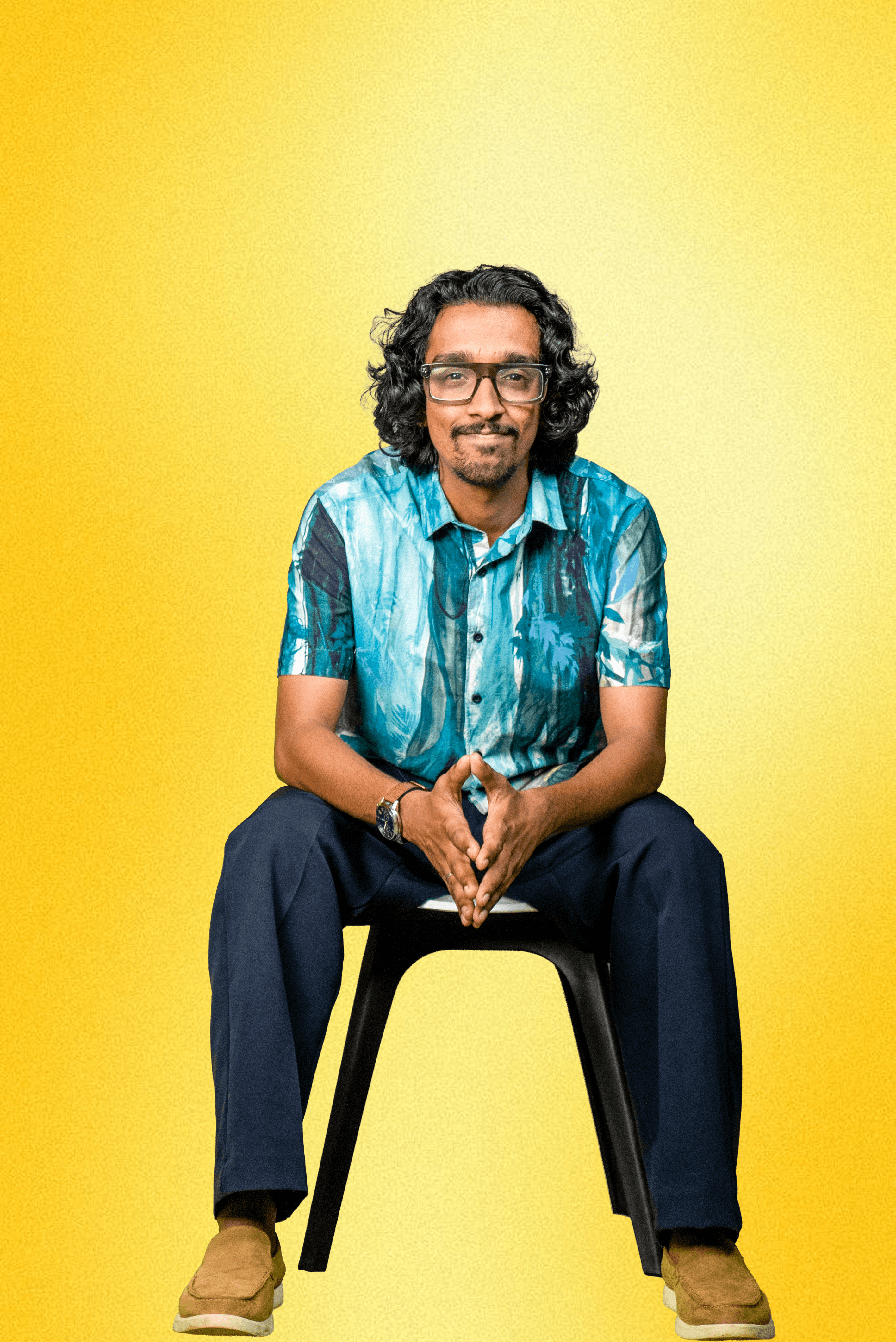 Asian man with glasses in a creative workspace, surrounded by colorful abstract art and stationery on a cluttered desk.