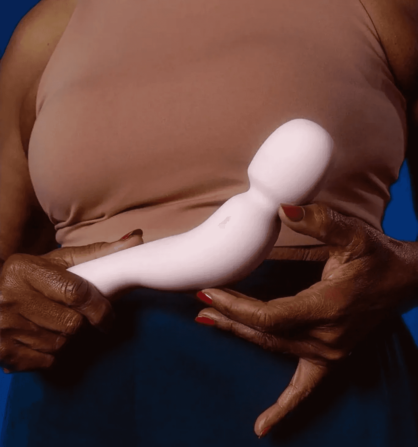 Person holding a pale pink Dame sexual wellness device against a brown top