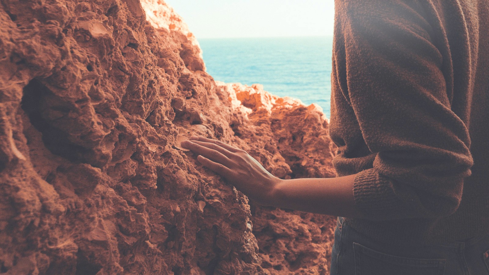 A traveler touching coastal rock formations by the sea in algarve, representing immersive, place-led journeys curated for multigenerational travel.