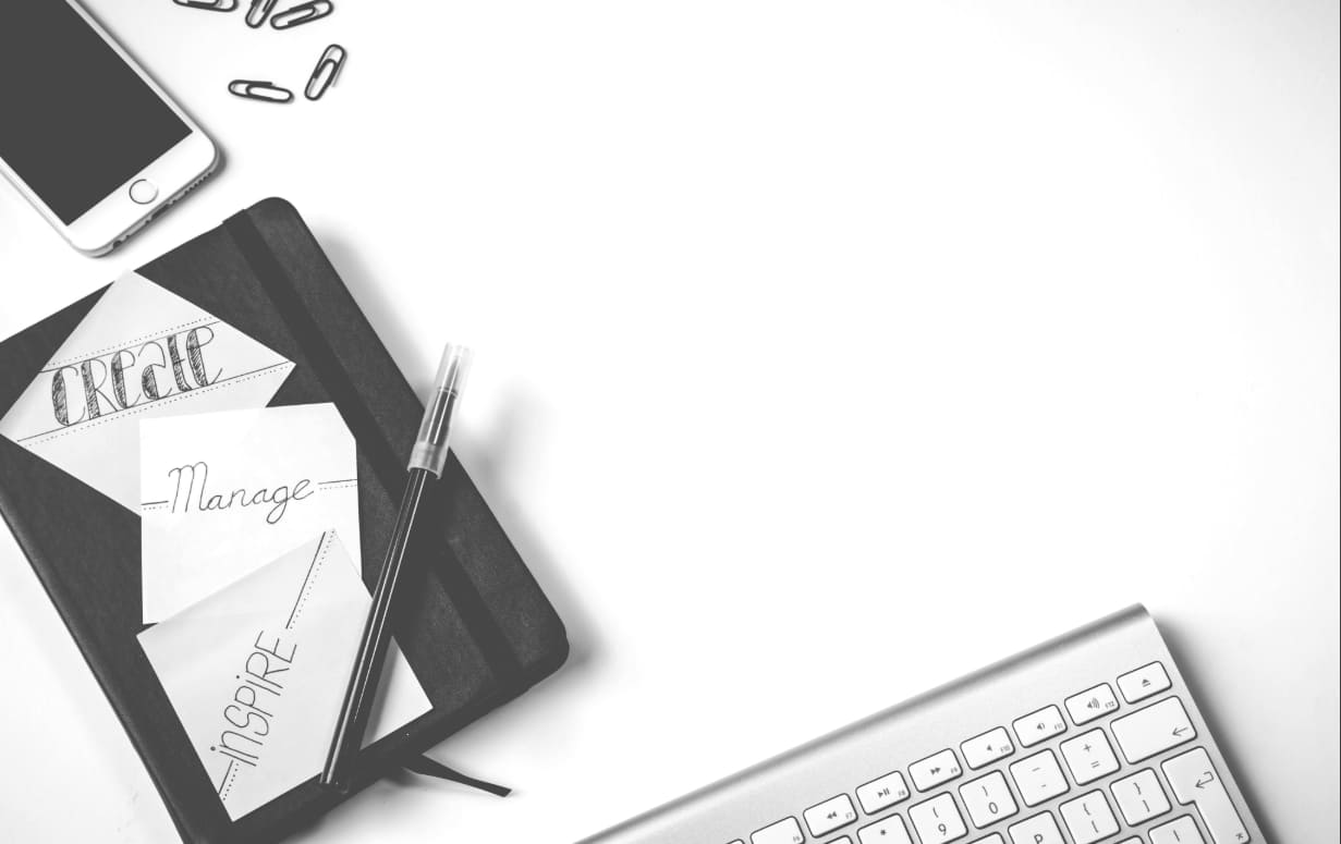 Workspace with notebook, pen, phone, keyboard, and paper clips. Handwritten words "create", "manage", and "inspire".