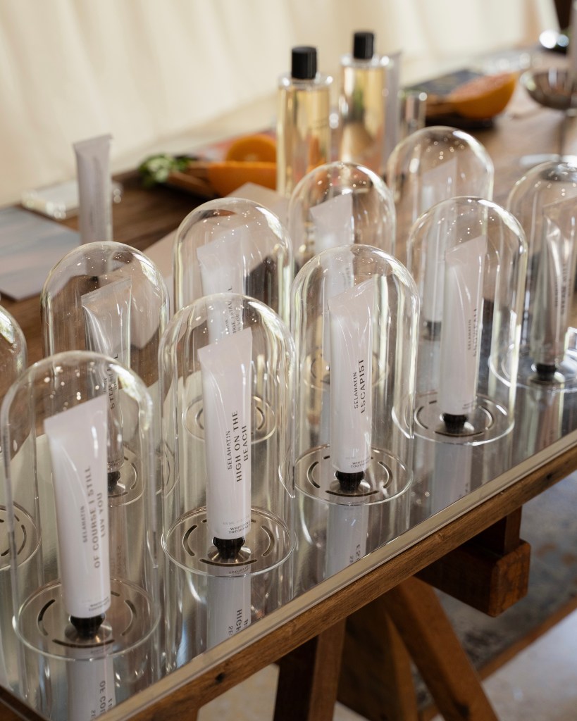 A display of skincare products under glass cloches on a wooden table, featuring various tube bottles with labels.