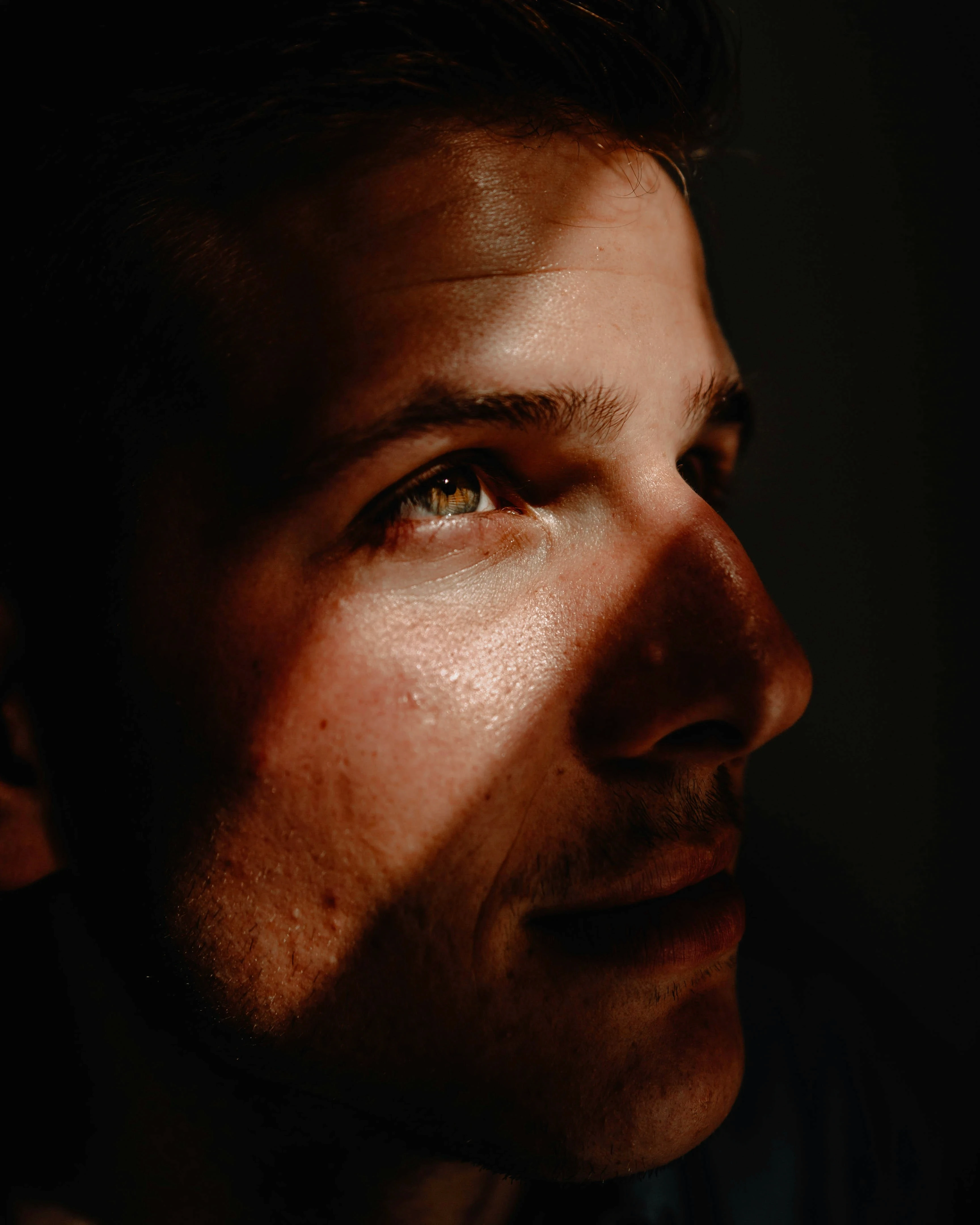 Close-up portrait of a man in dramatic light and shadow, gazing upward with a reflective, introspective expression, symbolizing inner struggle and emotional healing.