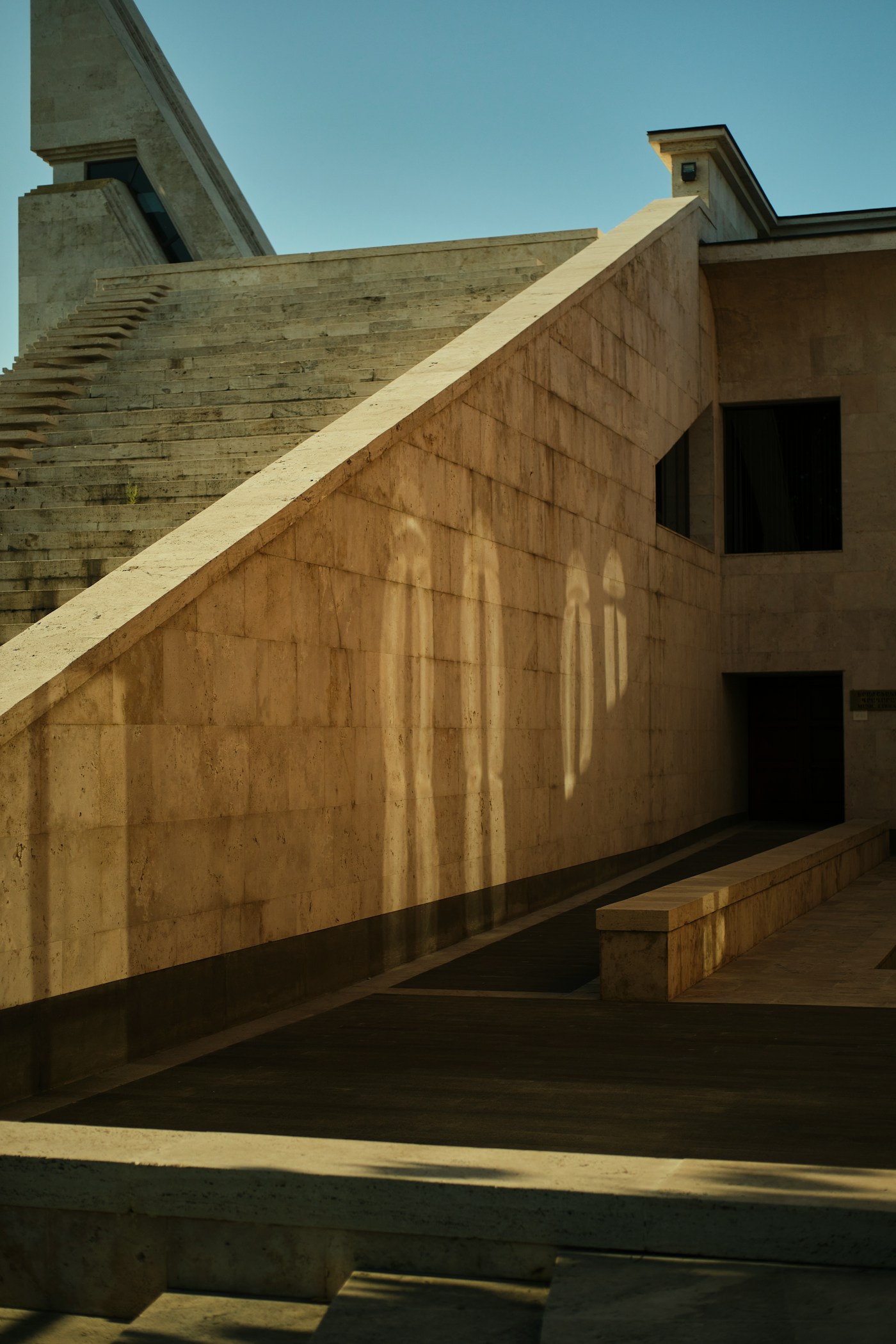 Warm stone architecture with sculptural stairs and strong geometric sunlight