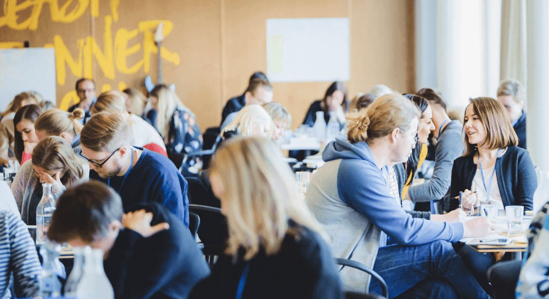 Large group of professionals collaborating at tables during a Design Sprint workshop training event