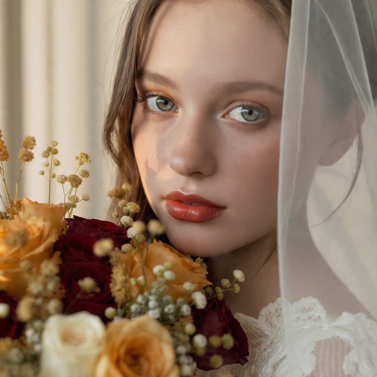Close-up of a bride with a veil holding a colorful rose bouquet.