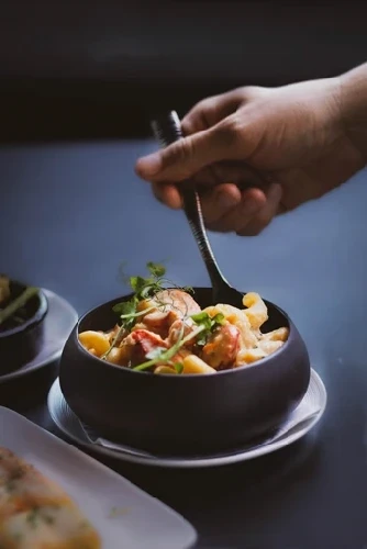 Hand using spoon to dish Lobster mac & Cheese