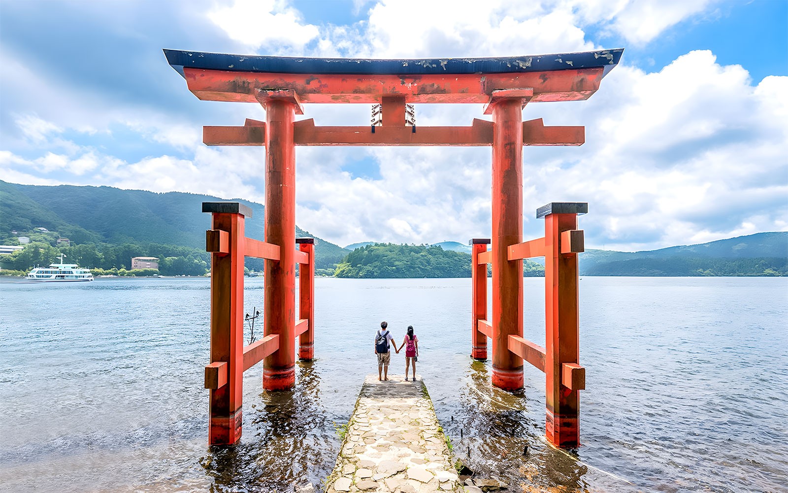 Egy pár áll a Hakone Torii kapunál, Ashi-tó, Japán, festői hegyi háttérrel.