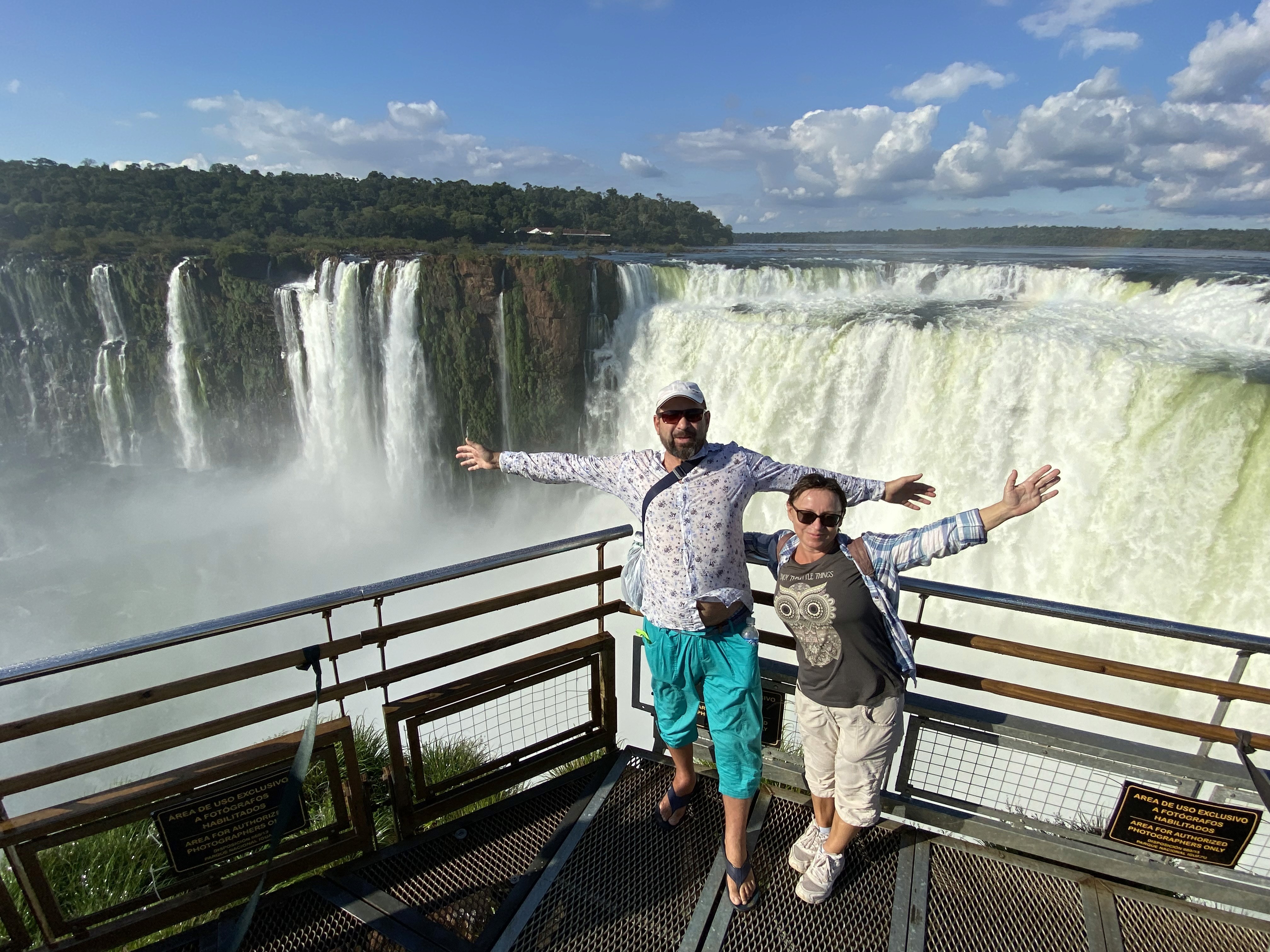 Mujer sentada sobre un tronco frente a una cascada doble en un bosque frondoso de Argentina.